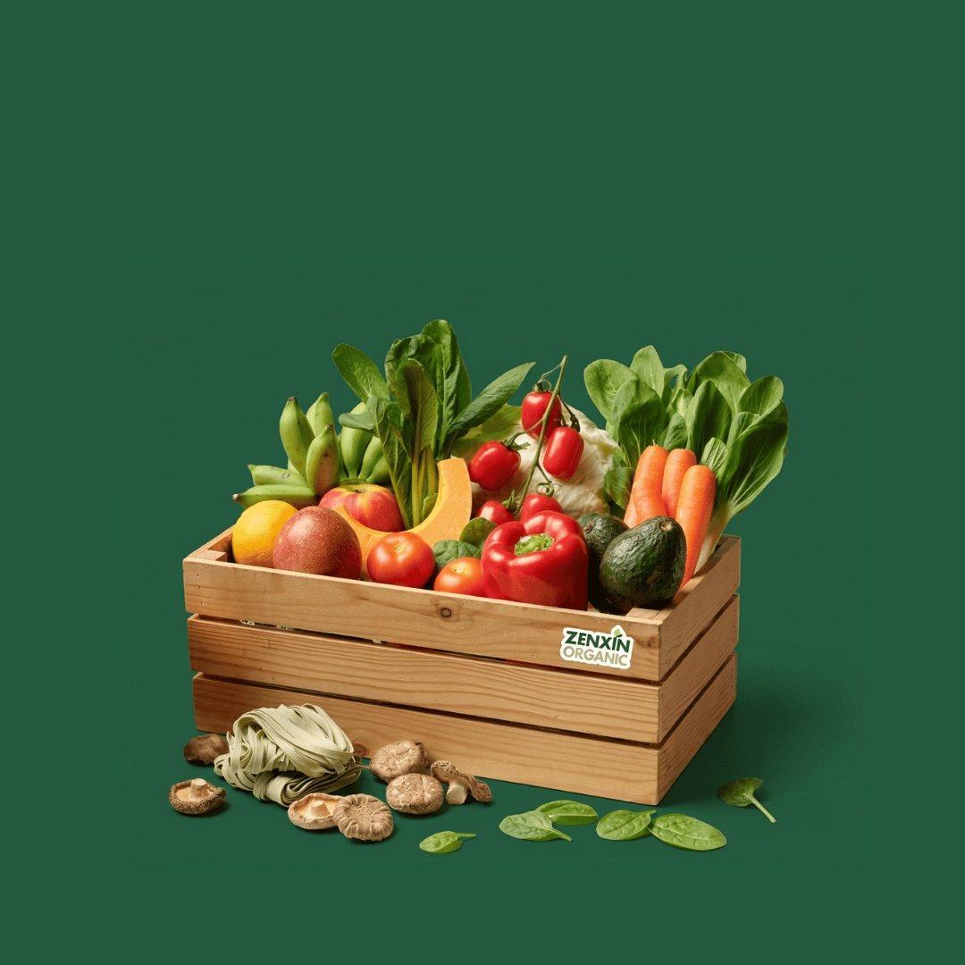 A wooden crate filled with fresh vegetables including tomatoes, carrots, spinach, broccoli, and an avocado, set against a solid dark green background. A small 'ZENAIN' brand sticker is visible on the front of the crate.