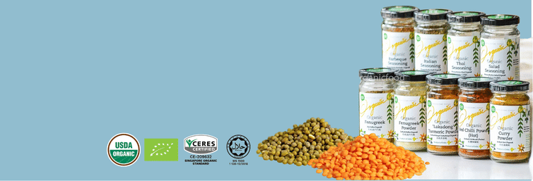 A group of glass jars of dried legumes and grains with white labels, displayed next to piles of green and orange dried lentils on a white surface, set against a solid light blue background. Several certification logos are visible on the left side of the image.